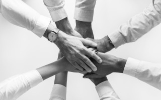 Six hands stacked one on another, in black and white